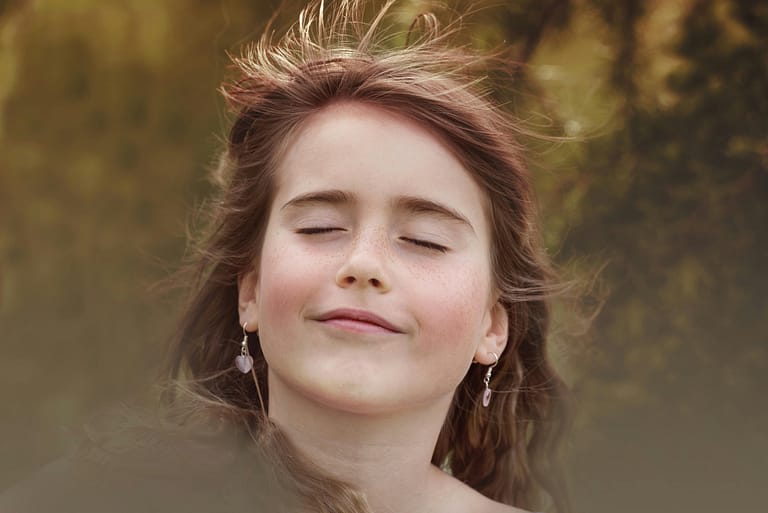 Portrait of a happy girl with closed eyes and wind-swept hair in a natural setting.